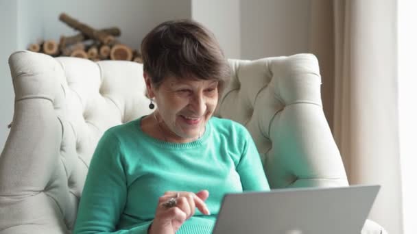 Happy elderly woman communicating by video call using laptop at home — Video Stock