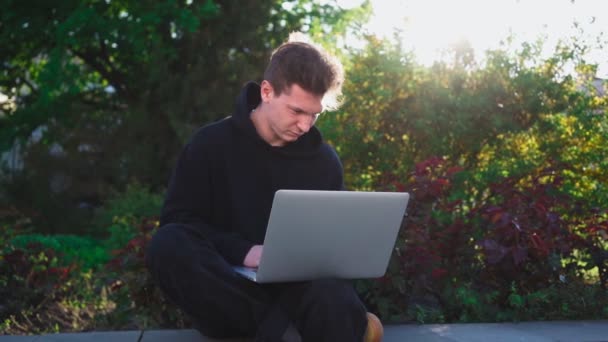 Killen jobbar på laptop i stadsparken. Manlig frilansare använder anteckningsbok för utomhusarbete — Stockvideo