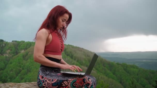 Kvinne frilanser arbeider bærbar på topp fjell-bakteppe praktfullt fjell – stockvideo