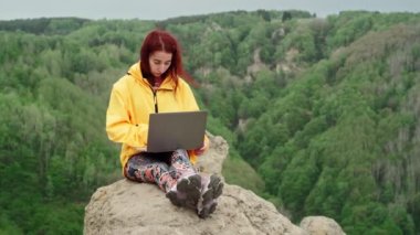 Serbest çalışan bir kadın, dağın tepesindeki muhteşem dağda dizüstü bilgisayarda çalışıyor.