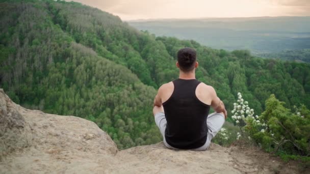 Человек практикует йогу и медитацию, сидя позицию лотоса на вершине горы — стоковое видео