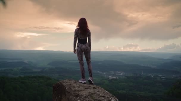 Atlétikai nő nyújtózkodik a lenyűgöző hegyi táj ellen. A lány spárgázik. — Stock videók