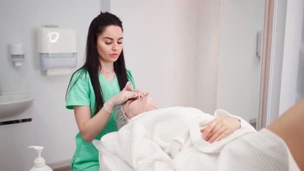 Жінка-косметолог робить процедуру догляду за шкірою обличчя жіночим пацієнтом в салоні краси — стокове відео