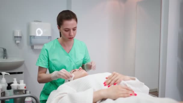 Chica esteticista hace procedimiento de limpieza facial para la mujer joven en el salón de belleza — Vídeo de stock