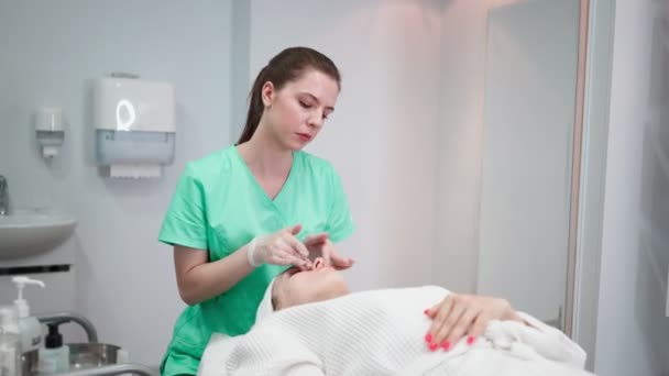 Dziewczyna kosmetyczka sprawia, że zabieg oczyszczania twarzy dla młodej kobiety w salonie piękności — Wideo stockowe