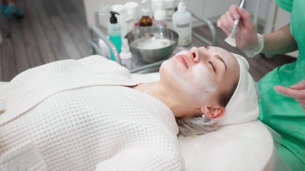 Dziewczyna kosmetyczka sprawia, że zabieg oczyszczania twarzy dla młodej kobiety w salonie piękności — Wideo stockowe