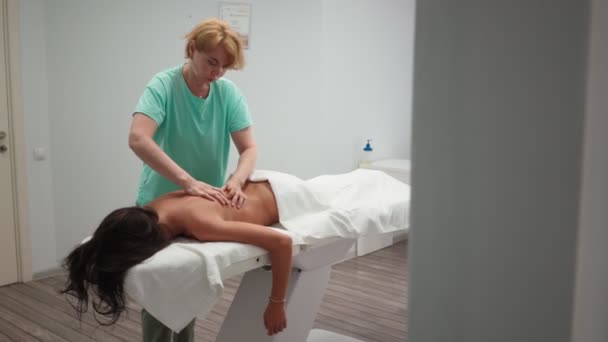 Массажист для взрослых делает лечебный массаж спины красивой девушкой в спа-салоне — стоковое видео