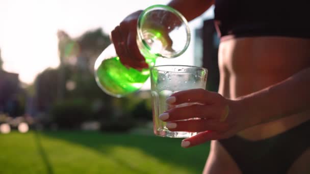 Schlanke Frau im Badeanzug gießt Erfrischungsgetränkestücke aus Flasche ins Glas — Stockvideo