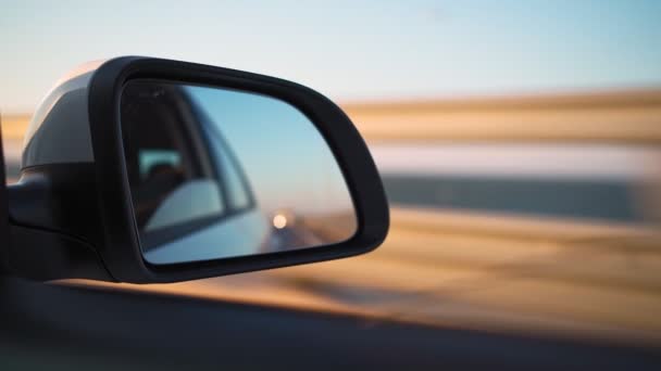 Ver en el espejo lateral del coche que está conduciendo rápido en la carretera en la luz del atardecer. — Vídeos de Stock