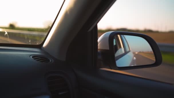 Ver en el espejo lateral del coche que está conduciendo rápido en la carretera en la luz del atardecer. — Vídeos de Stock