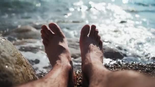 Beine unkenntlich Mann entspannt sich am Strand des Meeres an einem Sommertag. Urlaub und Reisen — Stockvideo