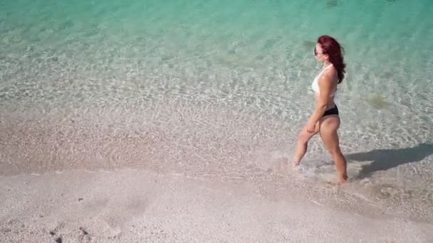 Gyönyörű lány fürdőruhában sétál az átlátszó türkiz tengeren a part mentén. — Stock videók