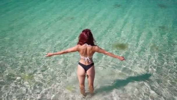 Красивая стройная девушка в купальнике поднимает руки, стоя в бирюзовом море — стоковое видео