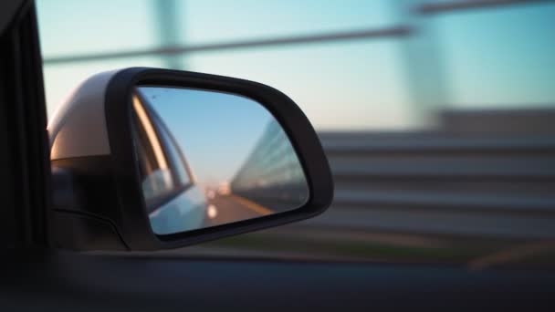 Ver en el espejo lateral del coche que está conduciendo rápido en la carretera en la luz del atardecer. — Vídeos de Stock