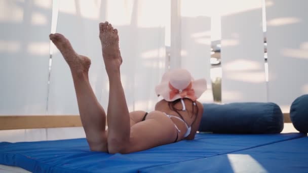 Ung slank kvinde i en hat slapper af, mens hun ligger i havepavillon. Sommertid. – Stock-video