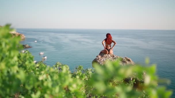 수영복을 입은 섹시 해 보이는 여자 가 해변에서 바위 위에 앉아 있다 — 비디오