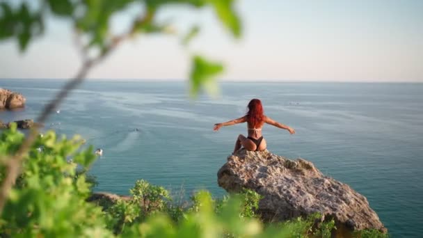 Femme en maillot de bain assis sur le rocher lève les mains vers le haut sentiment bonheur toile de fond mer — Video