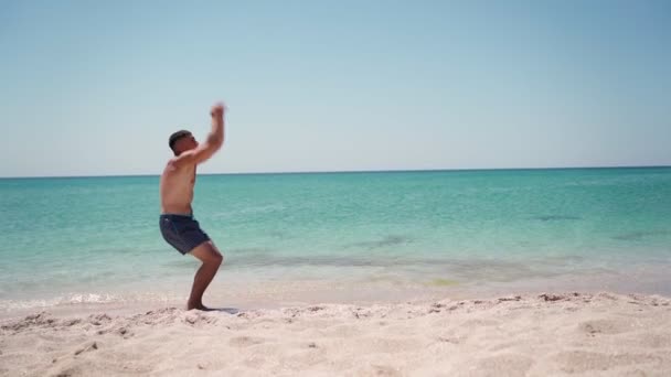Athletic man doing back flip on sea beach. Summer vacation concept. Slow motion — стоковое видео