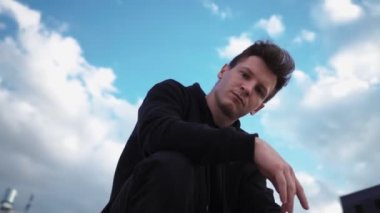 Siyah kapüşonlu şık adam şehir parkında oturur ve kameraya bakar. Yavaş çekim