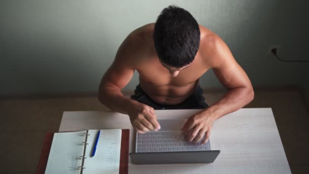 М'язистий чоловік голий до тулуба працює дистанційно на ноутбуці вдома. Віддалена робота — стокове відео