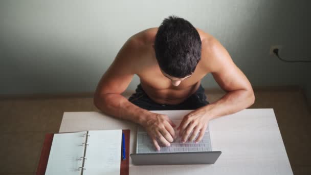 Gövdesine kadar çıplak olan kaslı adam evdeki dizüstü bilgisayarda çalışıyor. Uzak çalışma — Stok video