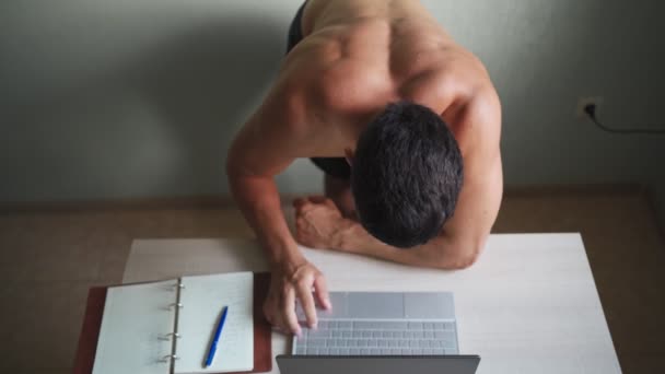 Мускулистый мужчина, обнаженный до туловища, работает дистанционно на ноутбуке дома. Дистанционная работа — стоковое видео