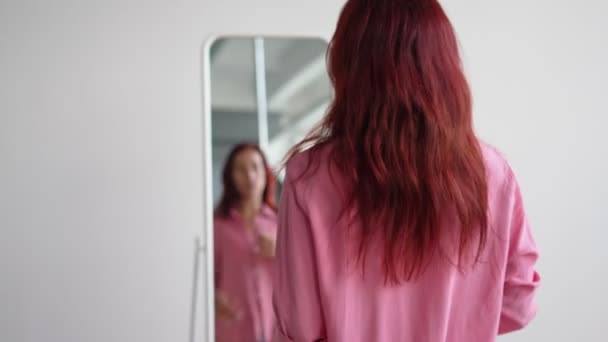 Desde la espalda, la mujer se pone la camisa rosa y preens delante del espejo en casa. — Vídeos de Stock