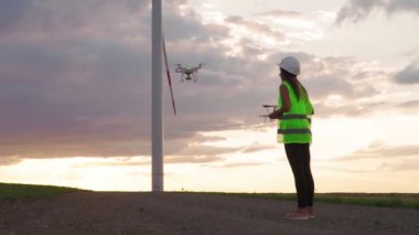 Üniformalı kadın mühendis elinde kumanda, uçan dron yel değirmeninde çalışıyor.