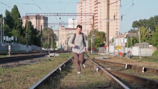 Ο ευτυχισμένος άντρας τρέχει στις γραμμές του τρένου και χαμογελάει, σηκώνοντας τα χέρια ψηλά. — Αρχείο Βίντεο