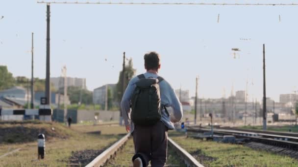 Feliz hombre corre a lo largo de las vías del tren y sonríe, levantando las manos — Vídeos de Stock