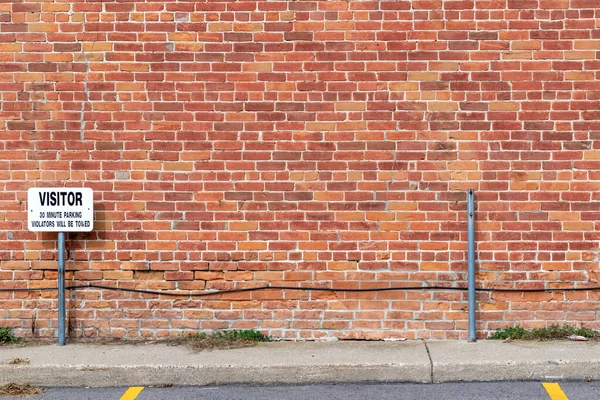 一般的な結合レンガ造りのパターンでアンティークグランジ赤茶色の粘土レンガの壁のテクスチャの背景は 訪問者の駐車記号と歩道のビューで 劣化と修復のセクションを示しています — ストック写真