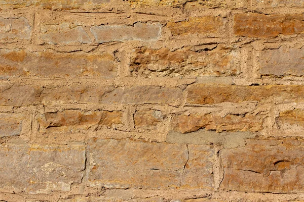 Full frame texture background of an antique golden brown stone wall with rough weathered surface in full sunlight