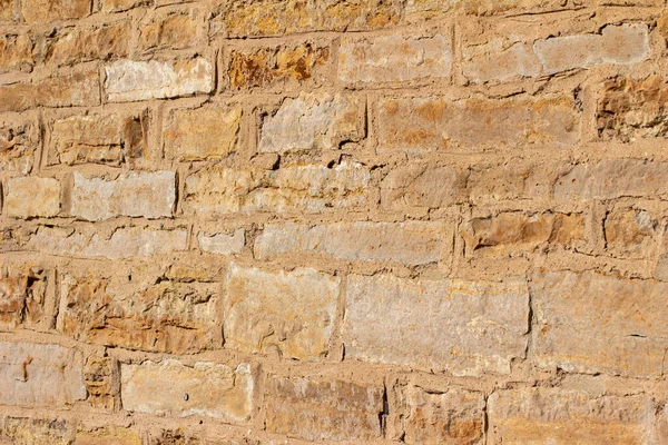 Full frame texture background of an antique golden brown stone wall with rough weathered surface in full sunlight