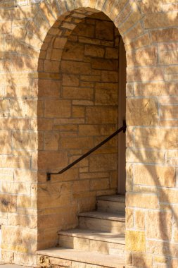 Dar kemerli kapı aralığı ve açık kahverengi renkli doğal taş blok duvar dokusu binasının girişine doğru adımlar Ashlar tuğla desenli doğal güneş ışığı ve yüzeyinde ağaç gölgeleri var.