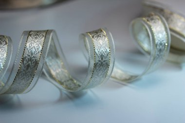 Beyaz arkaplanda, altın dikişli, ışıldayan gümüş desenli ipek kumaş kurdelesinin tam çerçeve makro dokusu.