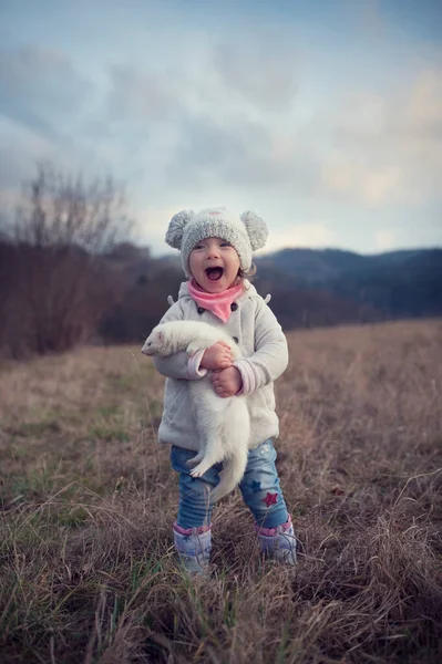 Küçük bir kız evcil hayvanıyla dışarıda. Elinde dağ gelinciği tutan tatlı bir bebek. Çocuk ve yaşayan tüylü hayvanı. Kırsalda sonbahar. Çocukların ve hayvanların arkadaşlığı. Yürümek...