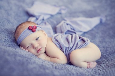 Yeni doğan bebek battaniyenin üzerinde uyur. Bebek için uyku zamanı. Güzel bantlı minik bebek yumuşak menekşe battaniyenin üzerinde yatıyor..