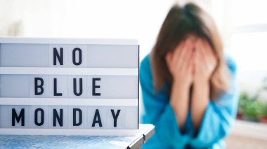 White board with text no blue monday on the table, in the background a woman in blue clothes depressed near the window,defocused.Blue monday day banner concept. Lettering clipart