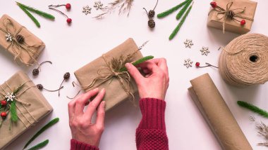 10.Adım adım çevre dostu ve sıfır atık Noel hediyesi paketi için adım adım. Kadın kahverengi kağıda sarılı bir hediye süslüyor ve canlı bitkilerle bağlanıyor, üst manzara, düz yatış