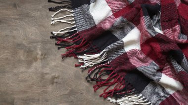 Kafeste yünlü kırmızı-siyah-beyaz ekose kumaş dokusu, kumaşın yakın çekimi, ahşap arka planda püskülleri olan kış tekstili, kopya uzay. Tartan kumaşı. Damalı desen..