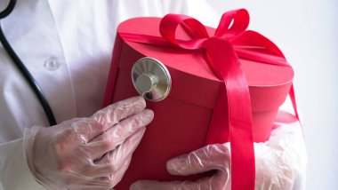 Noel ve yeni yıl tıbbi afişi. Beyaz önlüklü bayan doktor, steteskop, lateks eldivenli büyük kırmızı hediye kutusu, yakın plan. Doğum günü hediyesi, doktor günü, 8 Mart, anneler günü..