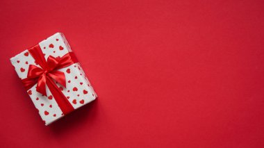 Sevgililer Günü afişi, kırmızı kalplerle beyaz kağıda sarılı hediye kutusu ve kırmızı arka planda kırmızı kurdele ile bağlanmış, üst manzara, düz yatak, fotokopi alanı, kutlama metinleri için yer..