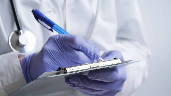 Close-up of a doctor writing a prescription in a medical record on a tablet. A doctor in a white coat and gloves is writing a prescription with a blue pen. Medical banner concept.