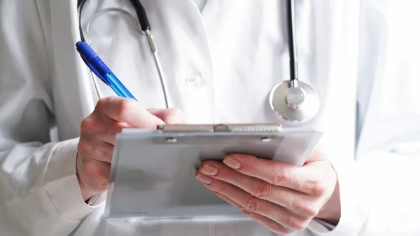 Close-up of a doctor writing a prescription in a medical record on a tablet. A doctor in a white coat writes a prescription with a blue pen. Medical banner concept.