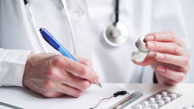 Doktor ellerinin bir tablete reçete yazıp reçete yazması. Beyaz önlüklü bir doktor elinde haplarla mavi kalemle reçete yazıyor. Tıbbi bayrak konsepti