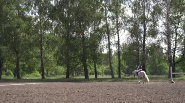 Binicilik spor yarışmasında beyaz atlı kız. Binicilik sınavı. Binicilik yarışmaları, at yarışları. Güneşli yaz gününde ata binen kız jokey. Ukrayna, Kiev 06.04.2021