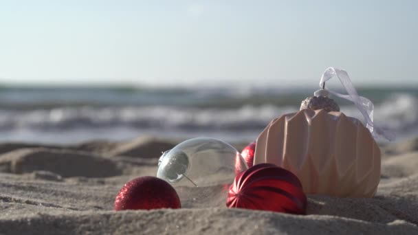 在蓝色的大海 大海的背景下 在沙滩上拍下了圣诞玻璃球的特写 圣诞节假期的概念或在温暖国家的海滩度假的概念 新年在海上度假 — 图库视频影像