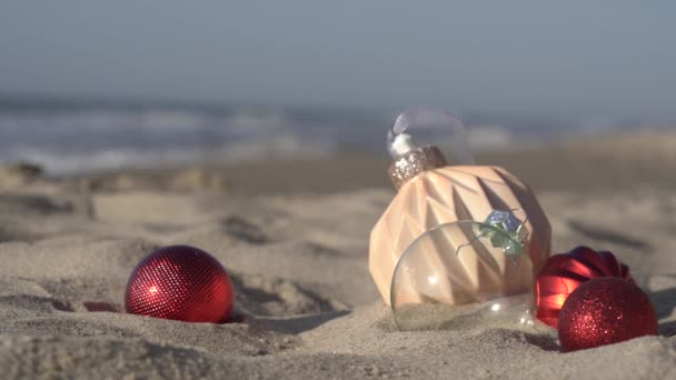 Κοντινό Πλάνο Χριστουγεννιάτικων Γυάλινων Σφαιρών Στην Άμμο Φόντο Γαλάζιας Θάλασσας — Αρχείο Βίντεο