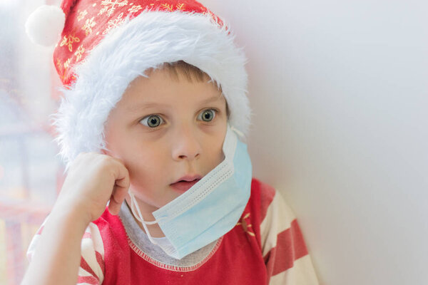 surprised boy in a santa hat takes off the medical mask. Close-up, soft focus, horizontal photo, without looking at the camera. End or tightening of isolation, bewilderment