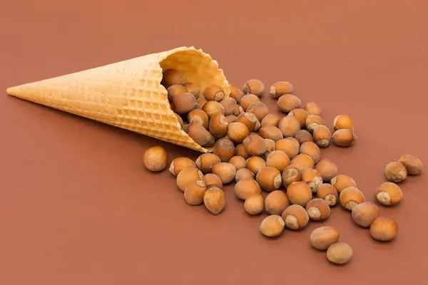 Hazelnuts pour out of the waffle cone. The idea is that the ice cream contains natural ingredients, nutty taste. Horizontal photo, brown background, close-up. — Stock Photo, Image